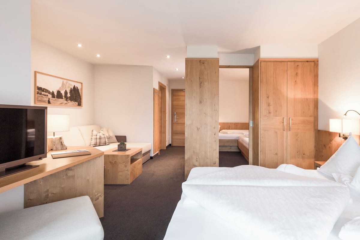 Een hotelkamer met een bed, een bureau met een computer, een televisie, een houten kledingkast en een schilderij aan de muur.