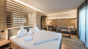 A modern hotel room with a large bed, a sofa, a desk, and a wooden wall. - Hotel Gasserhof Tradition & Lifestyle (Bressanone)