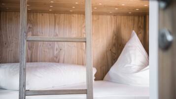 Una cama litera de madera con escalera, ropa de cama blanca y una pared de madera.