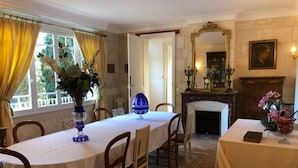 Een eetkamer met een ronde tafel, stoelen, een open haard en een spiegel.