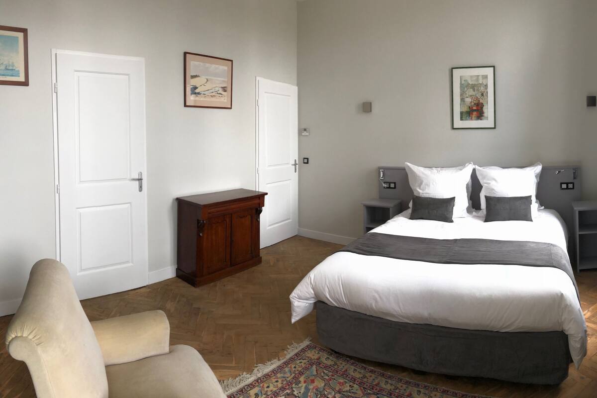 Une chambre à coucher comprenant un lit, deux tables de chevet, une chaise, une armoire en bois et trois tableaux encadrés accrochés au mur.