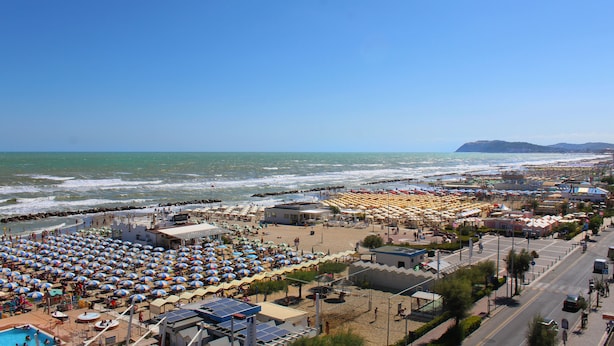 Een hotel aan het strand met meerdere kamers, een zwembad en strandparasols.