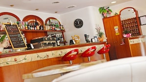 Een bar met een houten toonbank, rode barkrukken, een klok en diverse flessen en glazen.