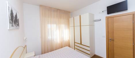 A bedroom with a bed, a wardrobe, a television, and a window with curtains.