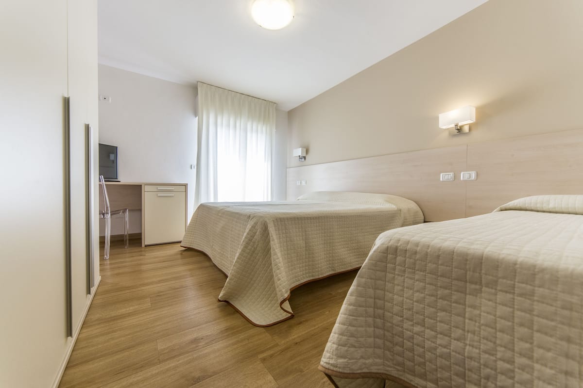 Une chambre d’hôtel avec deux lits, un bureau et une fenêtre avec des rideaux.