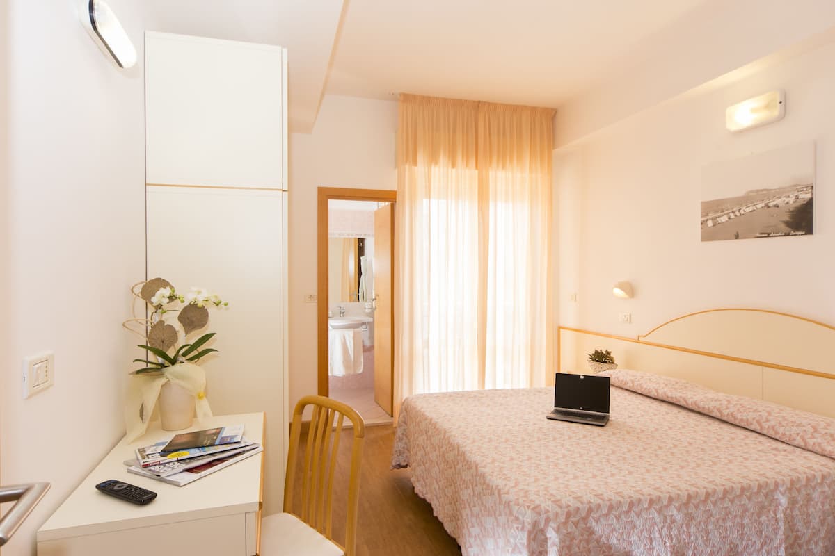 Une chambre d’hôtel comprenant un lit, un bureau avec un ordinateur portable, une chaise, une table de chevet avec un vase de fleurs et un miroir.