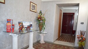 A hallway with a patterned floor, a glass-top table with a red box and figurines, a wicker basket with flowers, and a red door at the end. - B&B Villa Bellini (Catania)