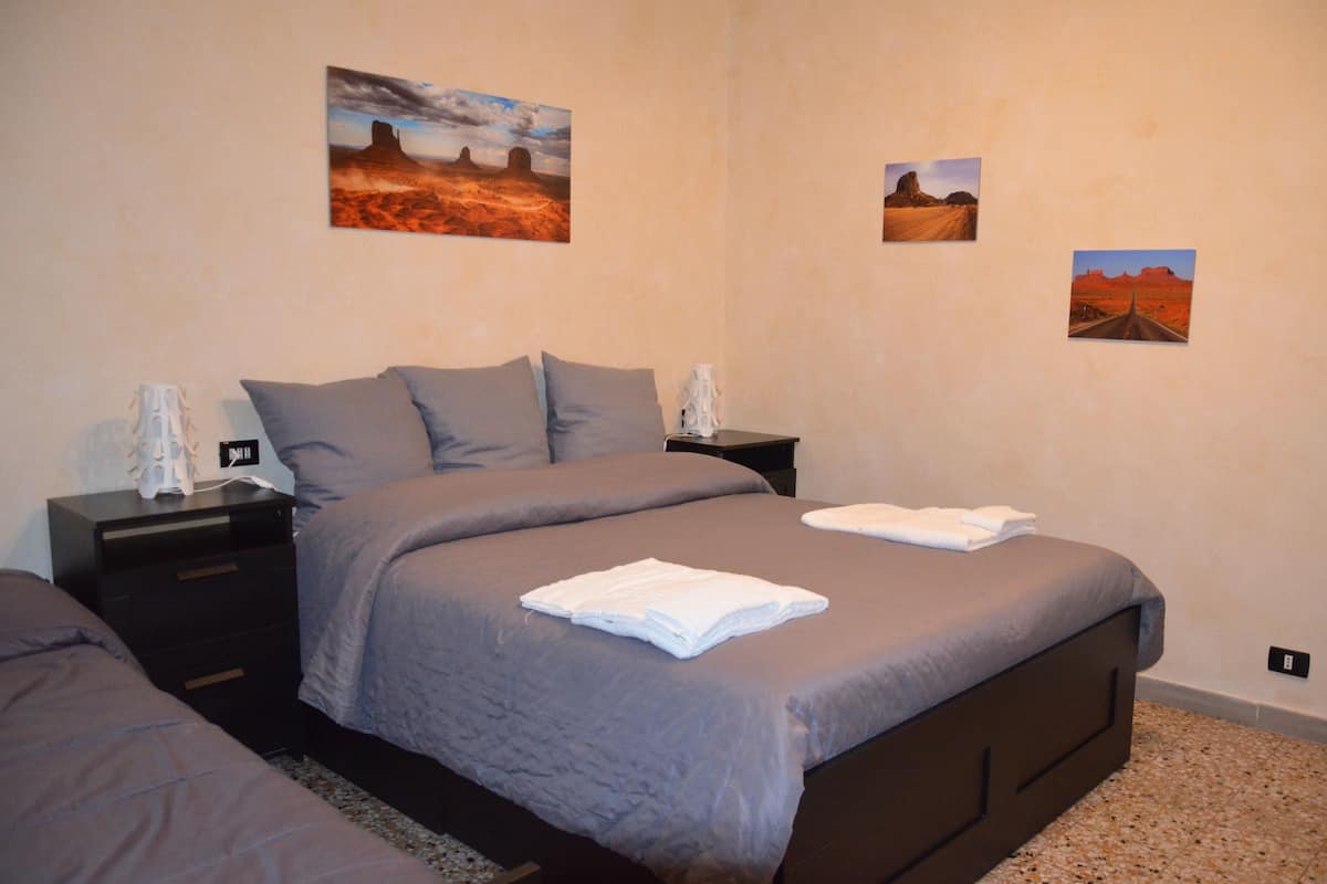 Un dormitorio con una cama grande, dos mesitas de noche y tres cuadros colgados en la pared que representan paisajes desérticos.