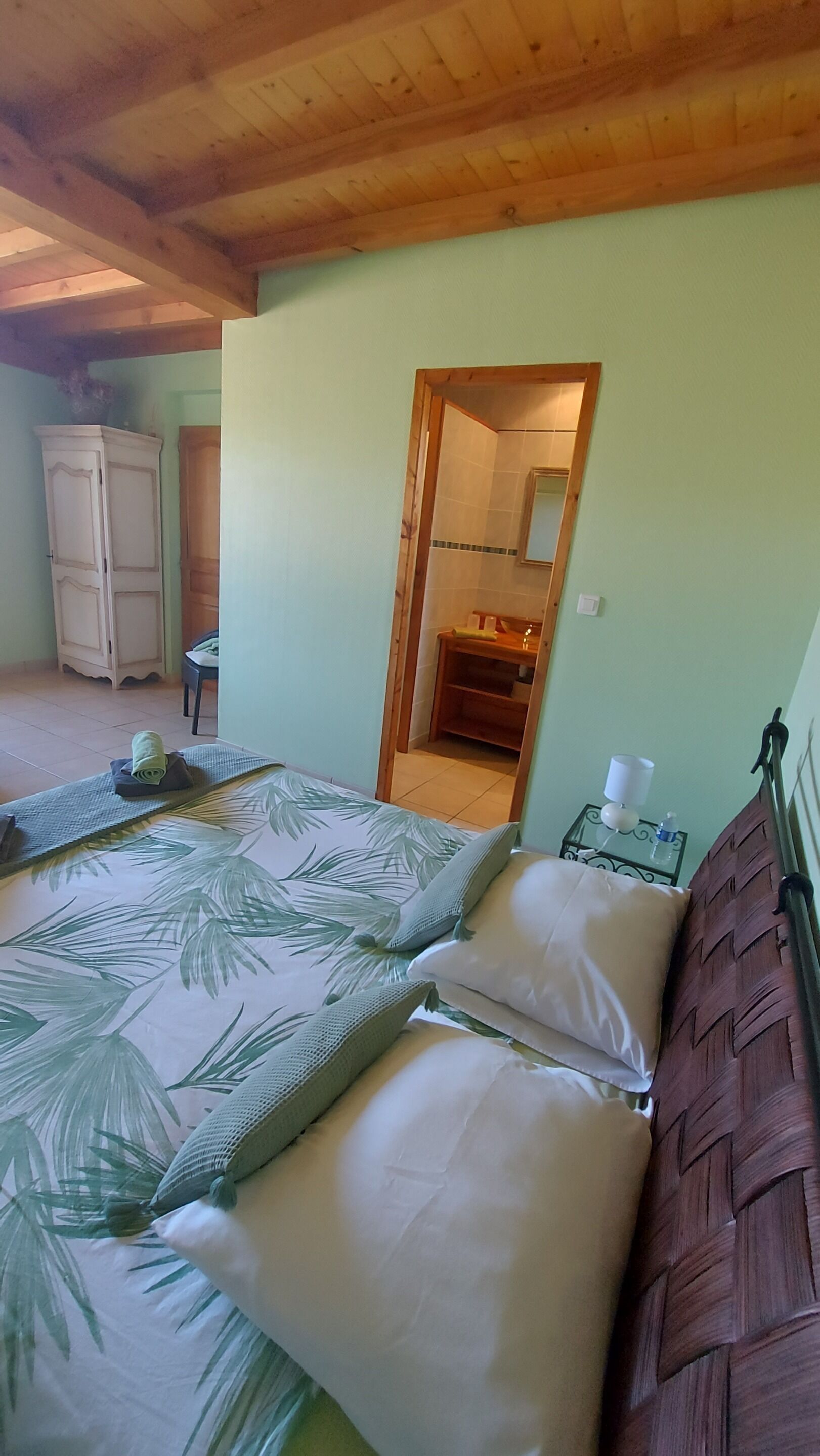 Un dormitorio con cama, mesita de noche, armario de madera y baño visible a través de una puerta abierta.