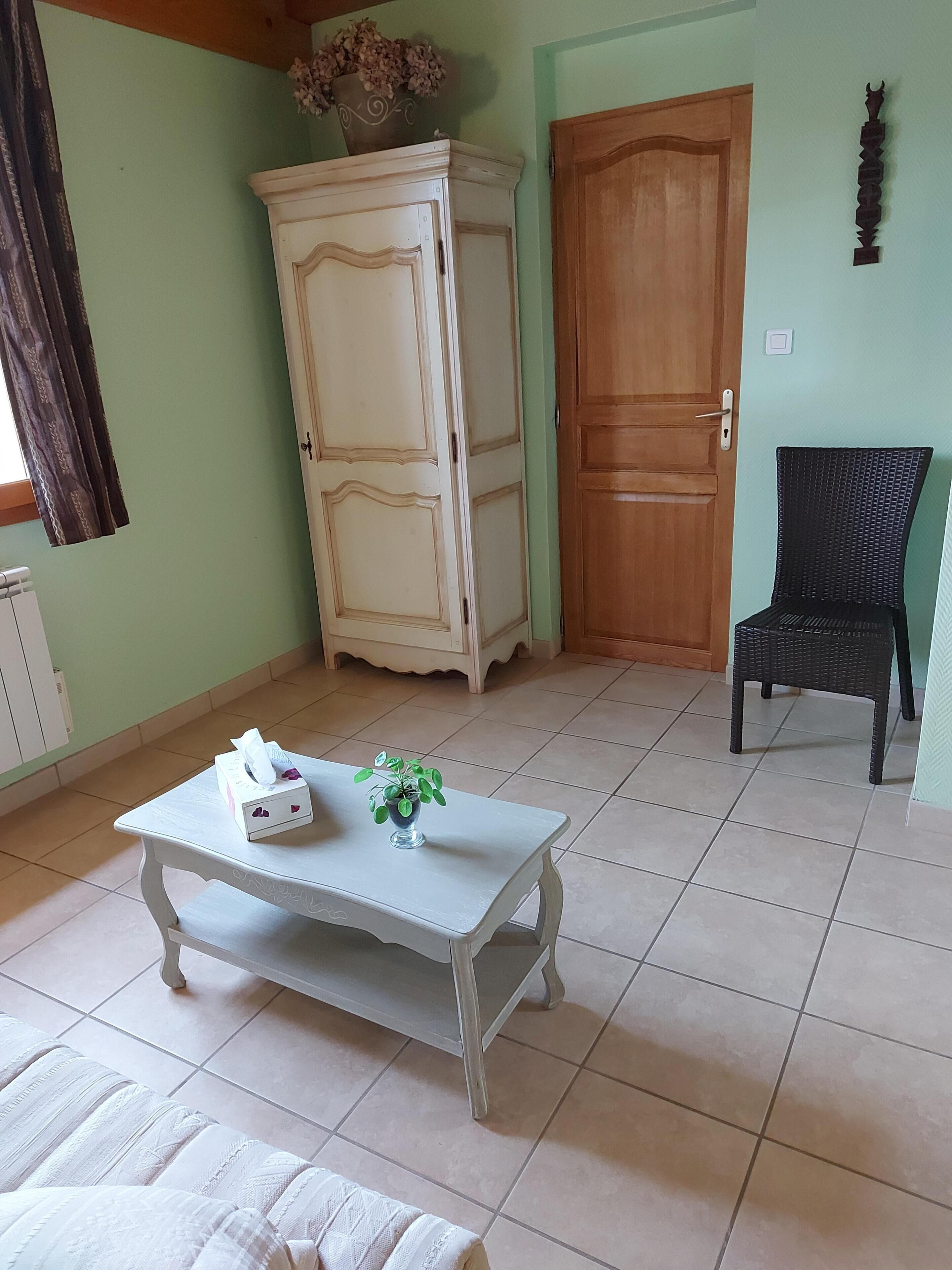 A room with a white table, a wicker chair, a wooden door, and a cabinet.