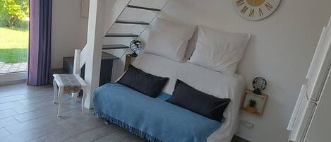 A modern bedroom with a bed, a small table, a clock, and a staircase.