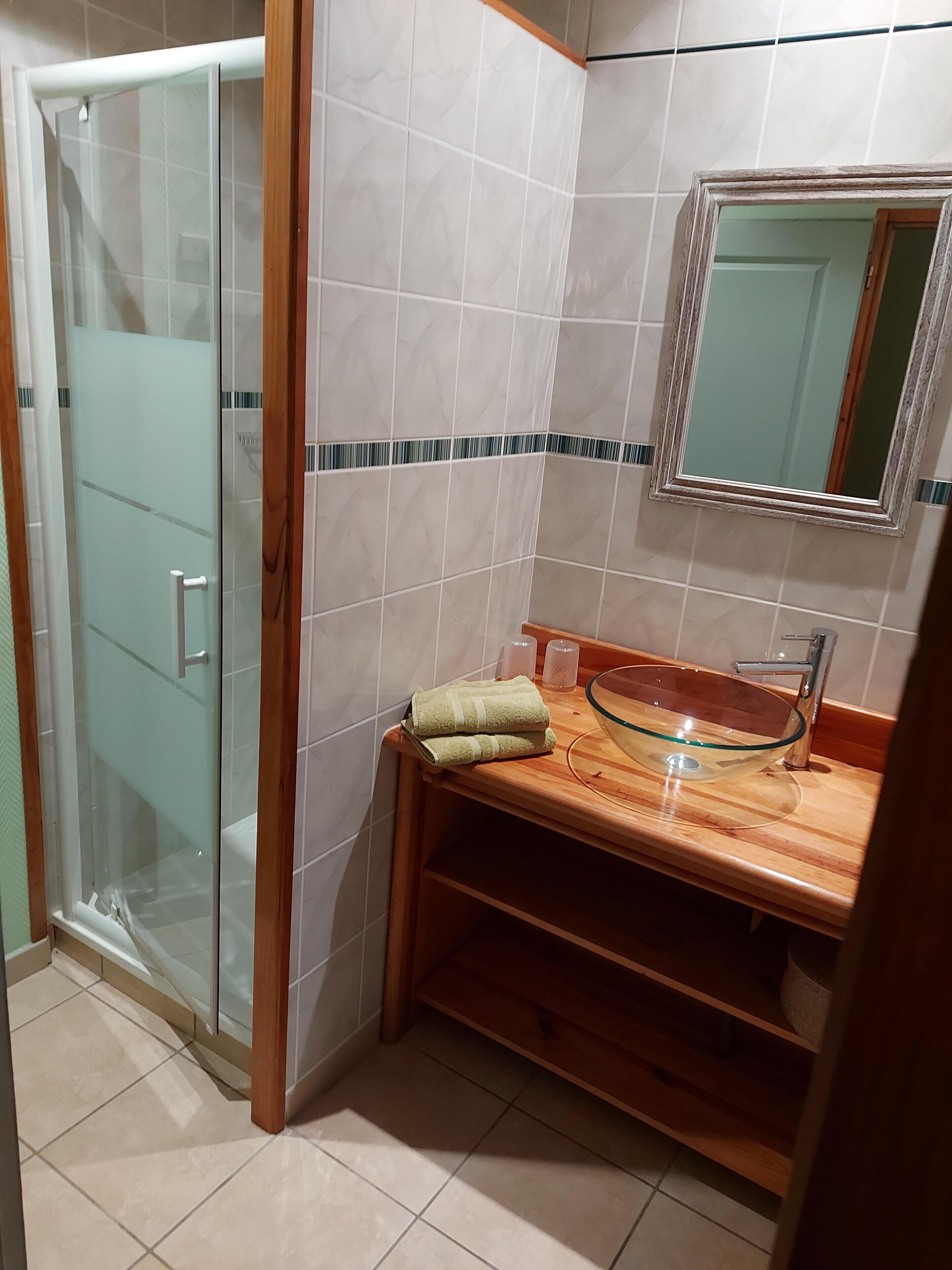 Un baño con cabina de ducha de vidrio, un mueble de tocador de madera con lavabo de vidrio y un espejo sobre el lavabo.