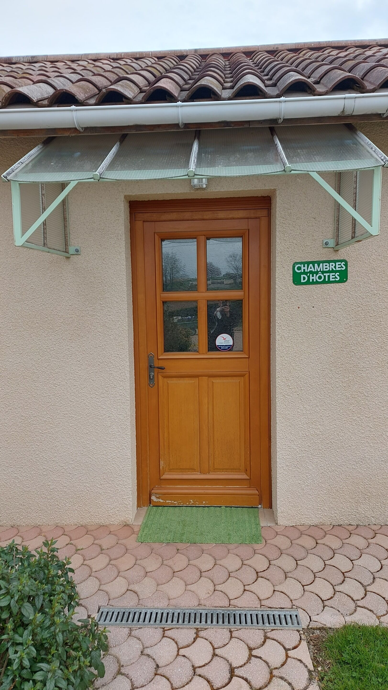 A wooden door with a green mat, a sign reading "CHAMBRES D HOTES", and a tiled roof.