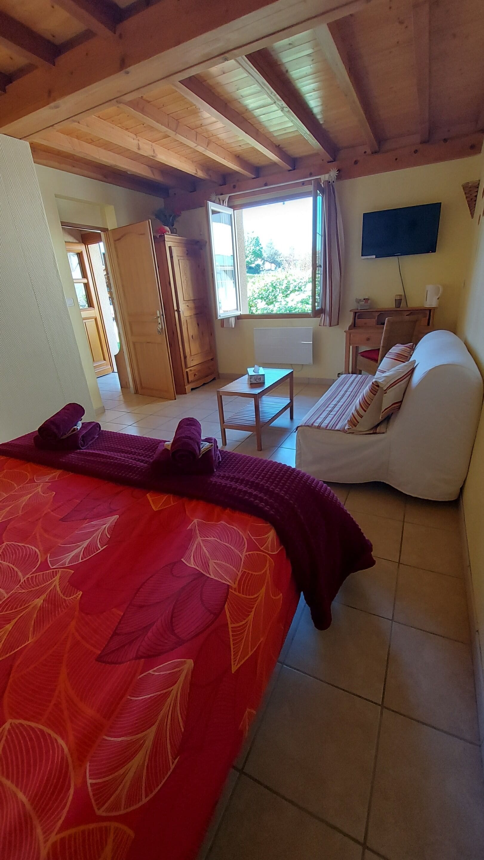 Una habitación con cama, sofá, una mesita, televisión y ventana con cortinas.