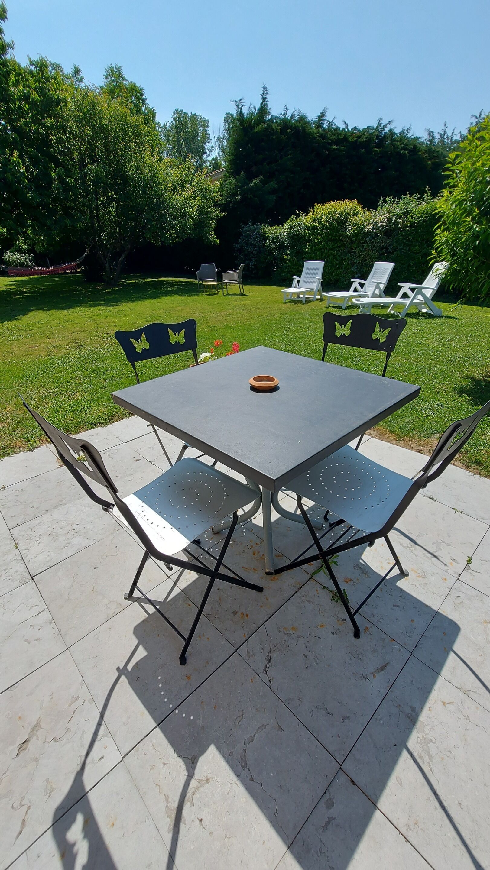 Una mesa cuadrada al aire libre con cuatro sillas, un cuenco pequeño y un jardín al fondo.