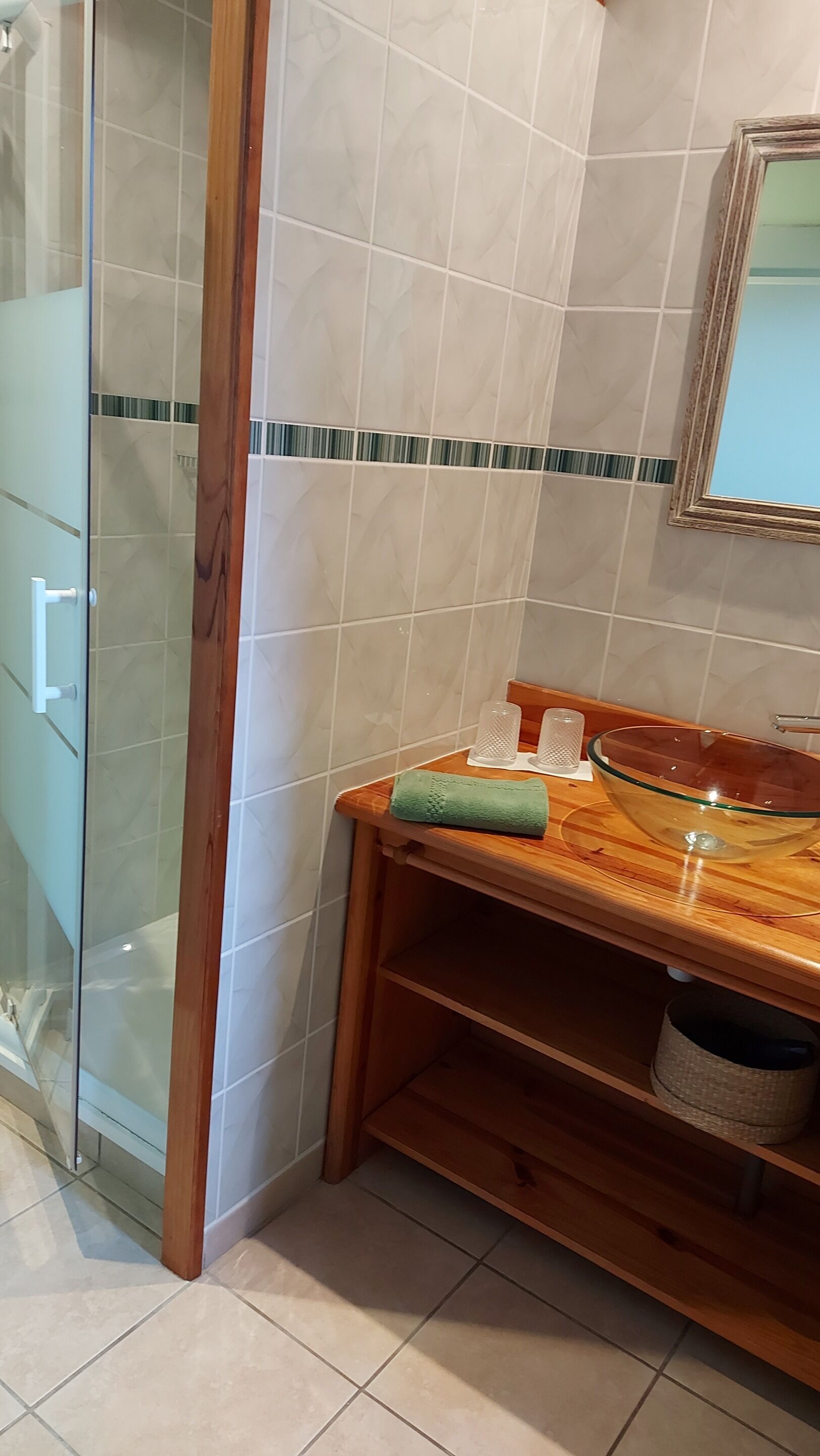 Un baño con cabina de ducha de vidrio, tocador de madera con lavabo y espejo sobre el lavabo.