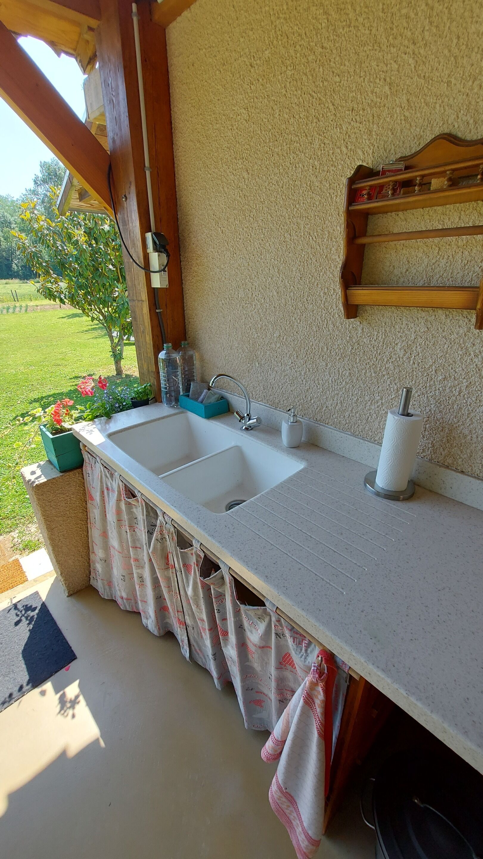 Une cuisine avec deux éviers, une étagère en bois où sont rangés divers objets, et une vue sur un jardin.