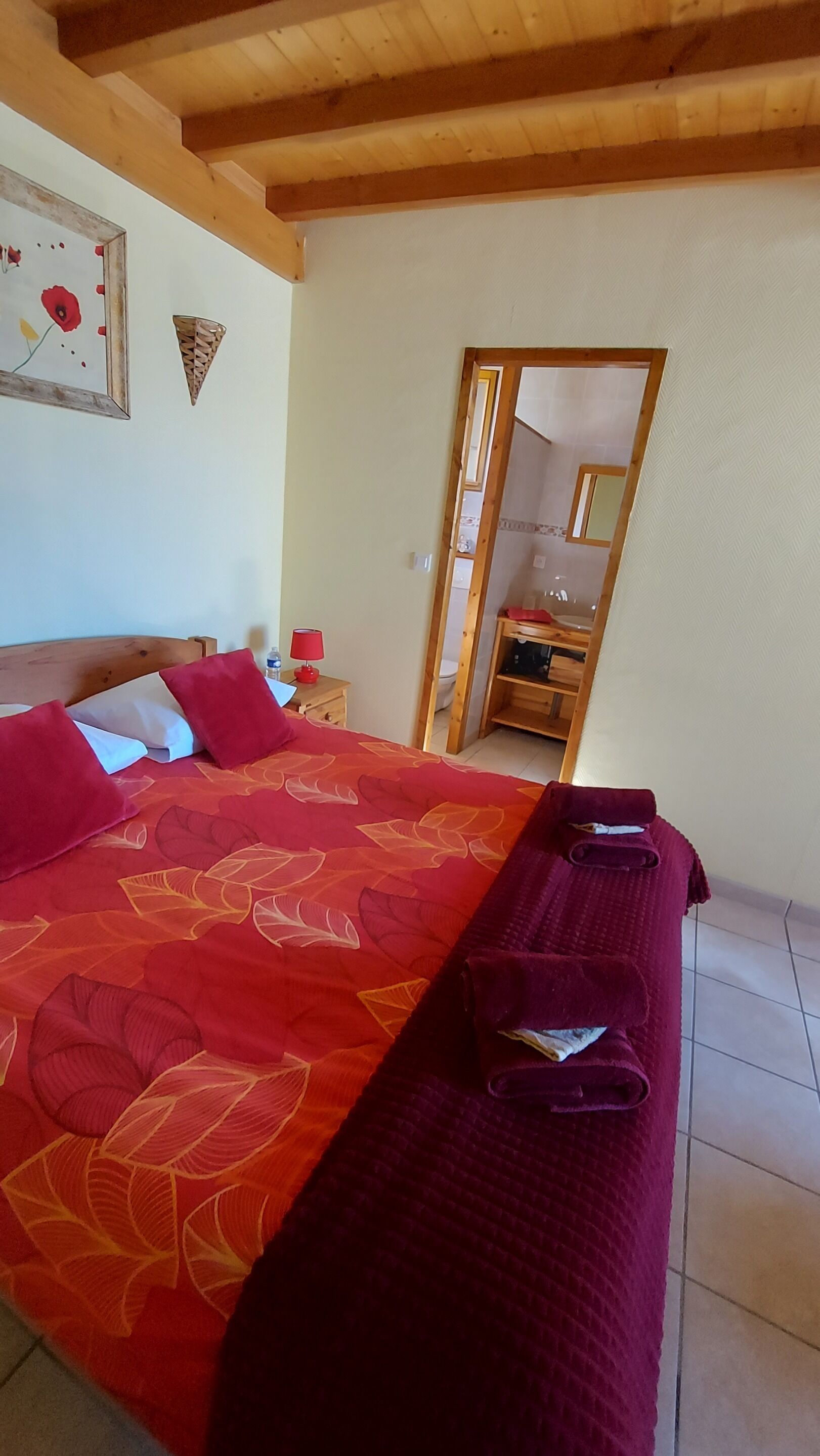 Un dormitorio con cama, mesita de noche, espejo y techo de madera.
