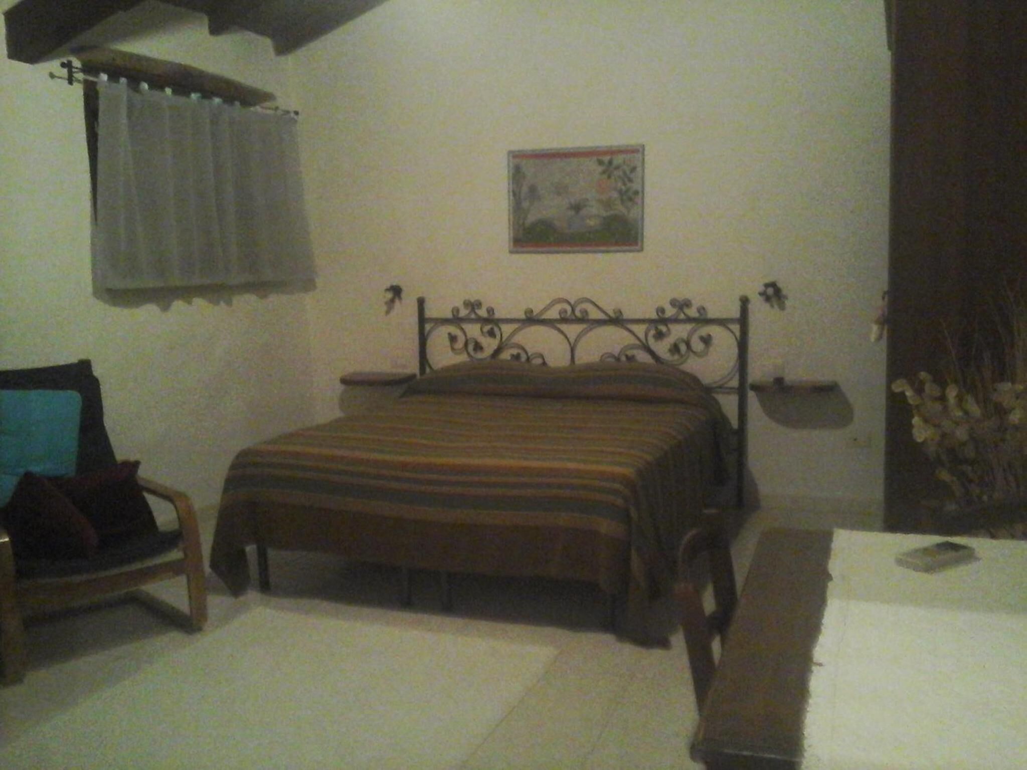 A bedroom with a bed, a chair, a table, and a wall-mounted picture.