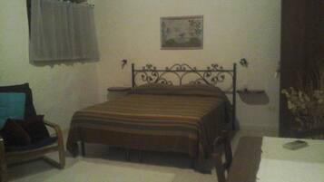 A bedroom with a bed, a chair, a table, and a wall-mounted picture.