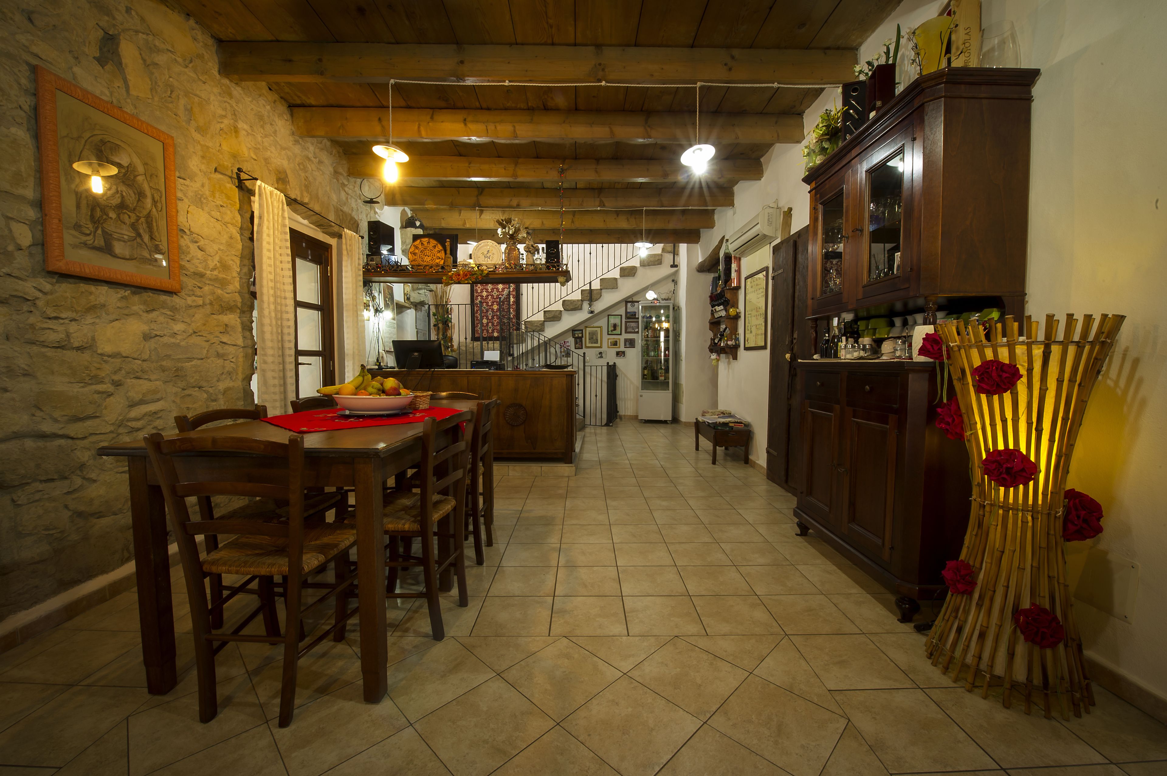 Un'area pranzo con un tavolo e sedie in legno, una scala che conduce a un livello superiore e un armadio in legno con diversi oggetti sopra.