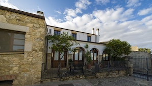 A stone building with a tiled courtyard, arched windows, and a metal fence. - Locanda La Rosa (Pauli Arbarei)