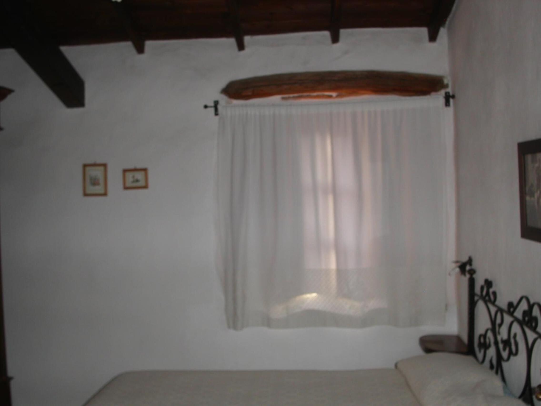 Een slaapkamer met een bed, een raam met een dunne gordijn en een houten plafond.