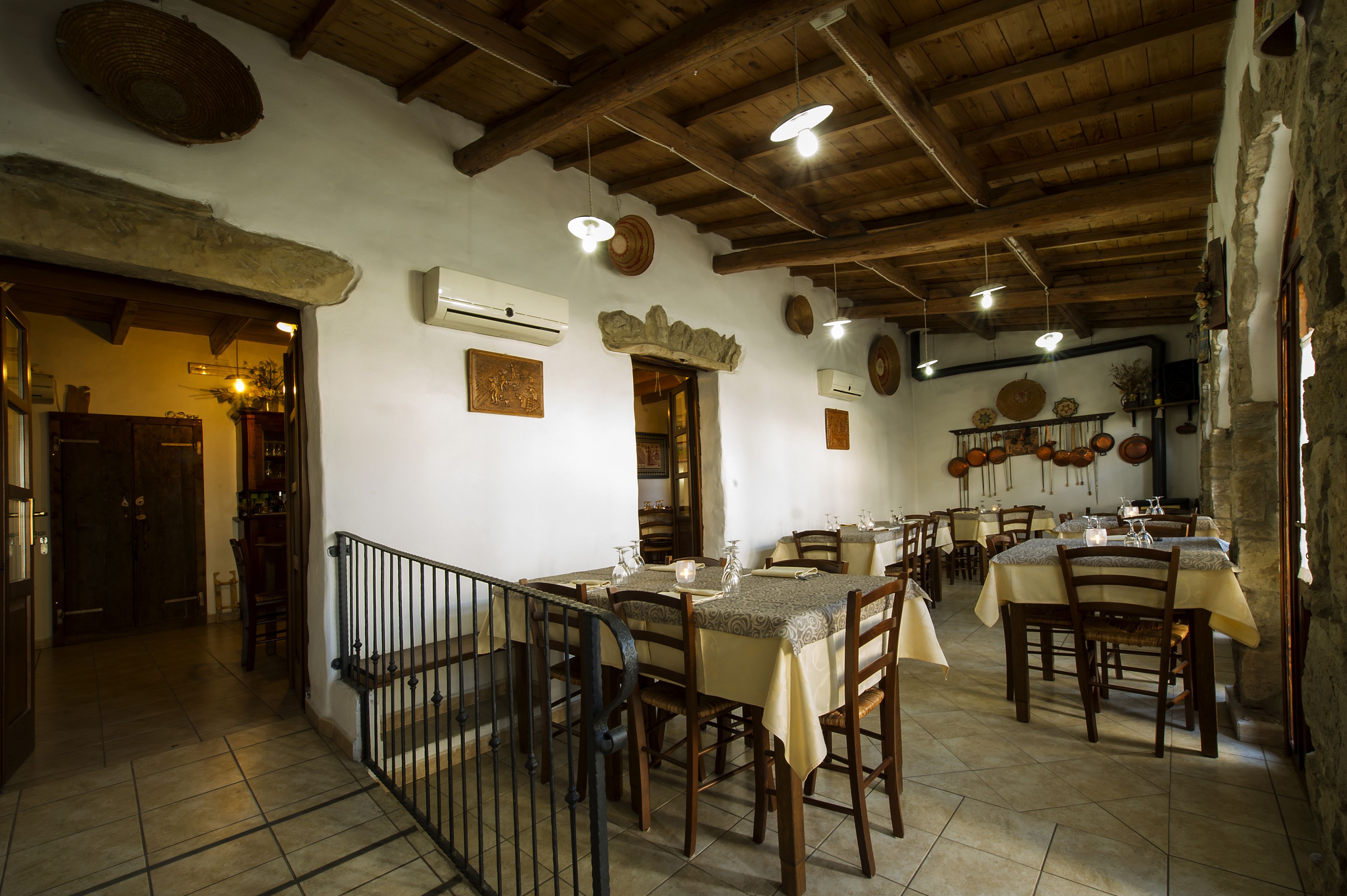 A rustic dining area with wooden tables and chairs, stone walls, and exposed wooden beams.