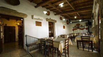 A rustic dining area with wooden tables and chairs, stone walls, and exposed wooden beams.