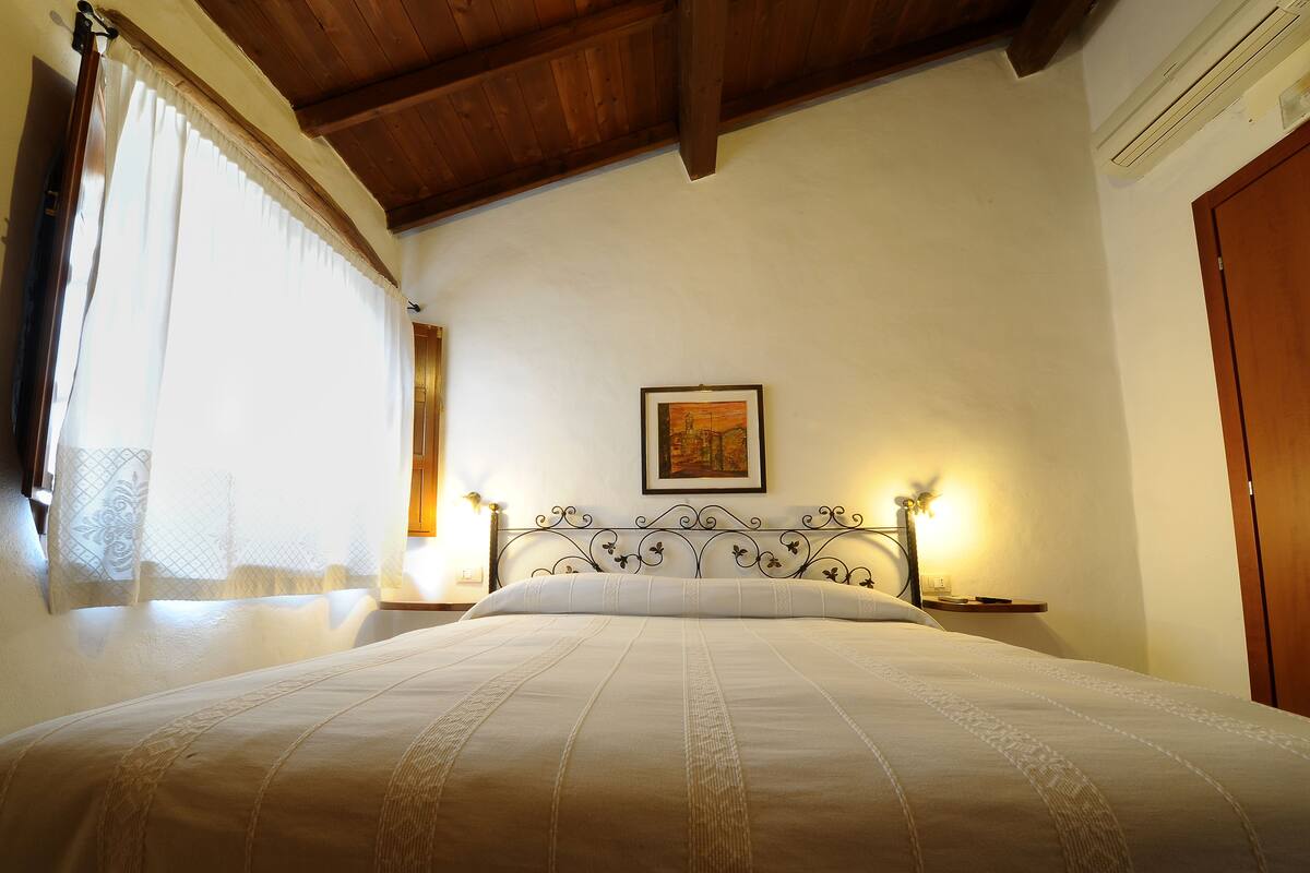 A neatly made bed with a headboard, a bedside table with a lamp, and a framed picture on the wall.