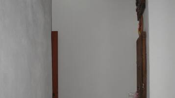 A narrow hallway with a wooden door on the right, a light fixture on the ceiling, and a chair on the left.