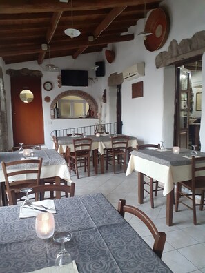 A dining area with multiple tables and chairs, a wooden ceiling, and a brick wall with a mirror and decorative plates.