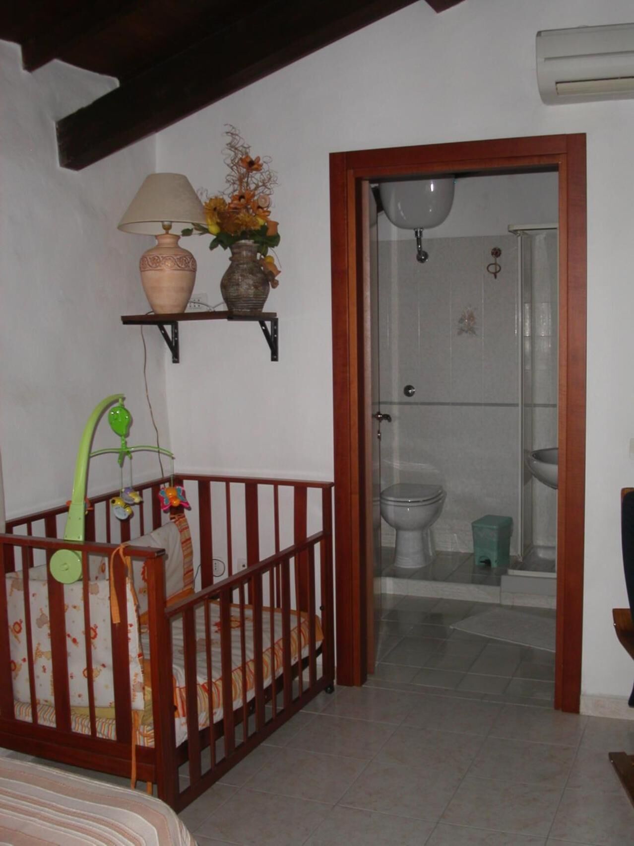 A room with a crib, a shelf with decorative items, and a shower area.