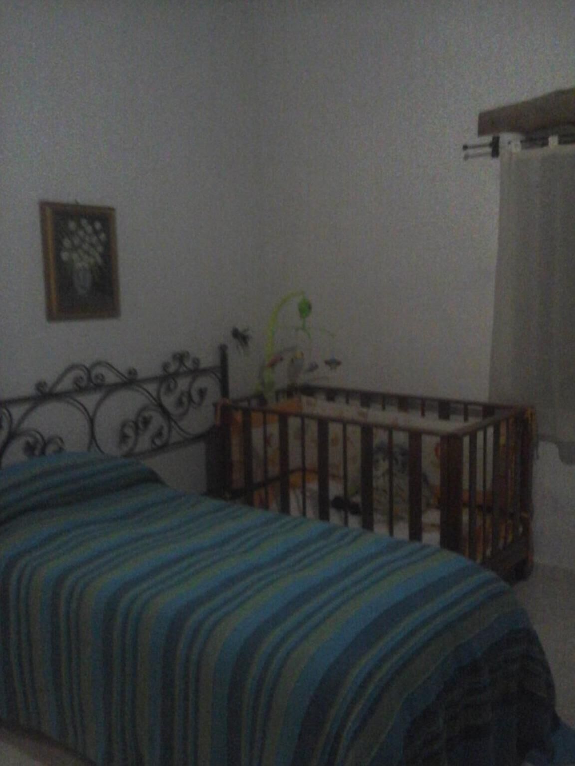 A bedroom with a bed, a crib, a framed picture on the wall, and a window with a curtain.