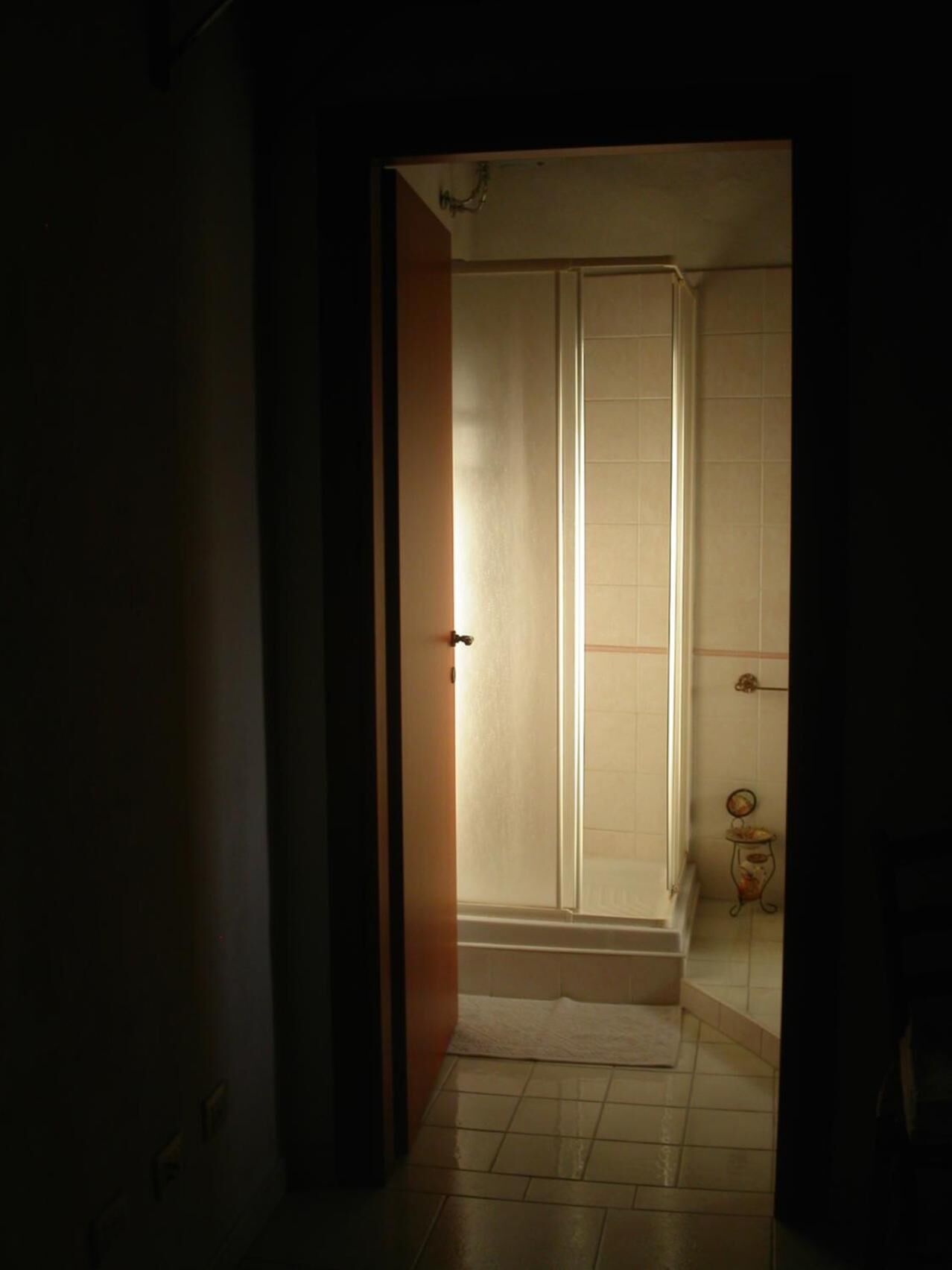 Un estrecho acceso que conduce a un baño con zona de ducha, paredes con azulejos y una pequeña mesa con espejo.