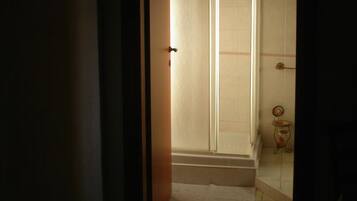 Un estrecho acceso que conduce a un baño con zona de ducha, paredes con azulejos y una pequeña mesa con espejo.