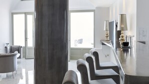 A modern hotel lobby with a marble floor, a large pillar, and a seating area with cushioned chairs. - Anchor Suites (Santorini)