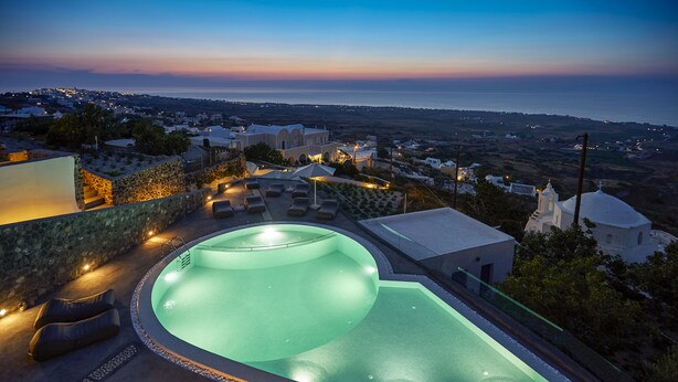 A swimming pool with a curved design, surrounded by lounge chairs and a stone wall. - Anchor Suites (Santorini)