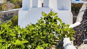 A white church with a bell tower and crosses, surrounded by greenery and a stone wall. - Anchor Suites (Santorini)