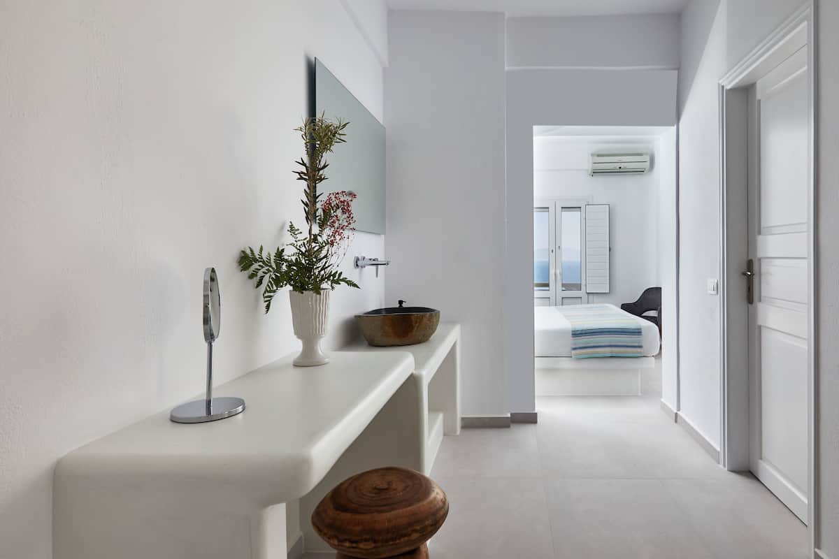 Un baño moderno con un tocador blanco, un taburete de madera, un espejo y una planta.