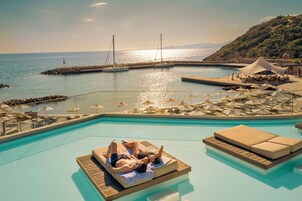 A pool area with lounge chairs and umbrellas, a view of the sea, and a rocky shoreline.