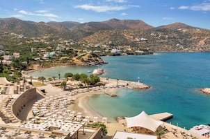 A coastal resort with a beach, lounge chairs, and a view of the sea and mountains.