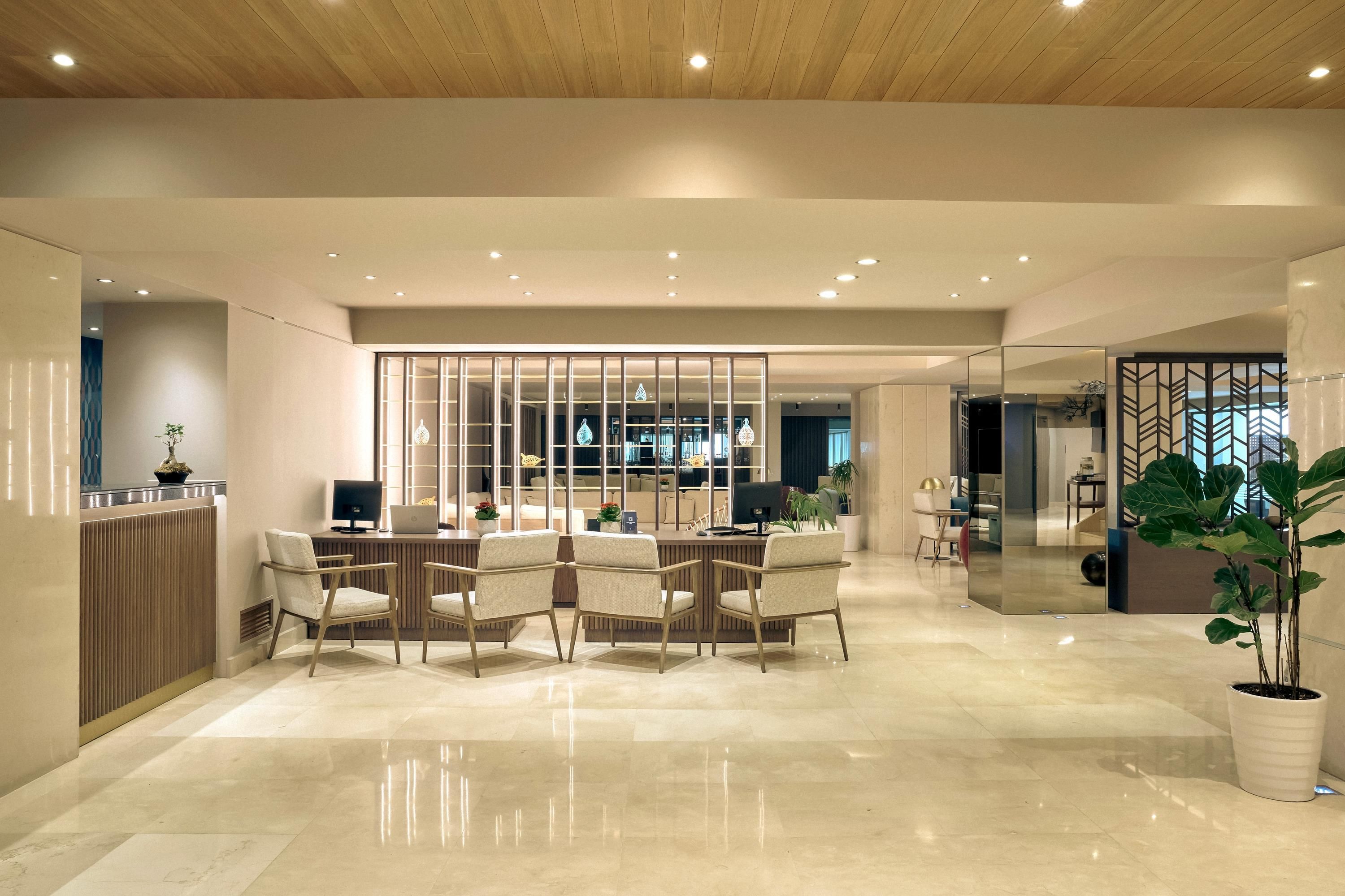 Un interior moderno con un comedor que cuenta con una mesa y sillas de madera, una cocina al fondo y un espejo grande que refleja el espacio.