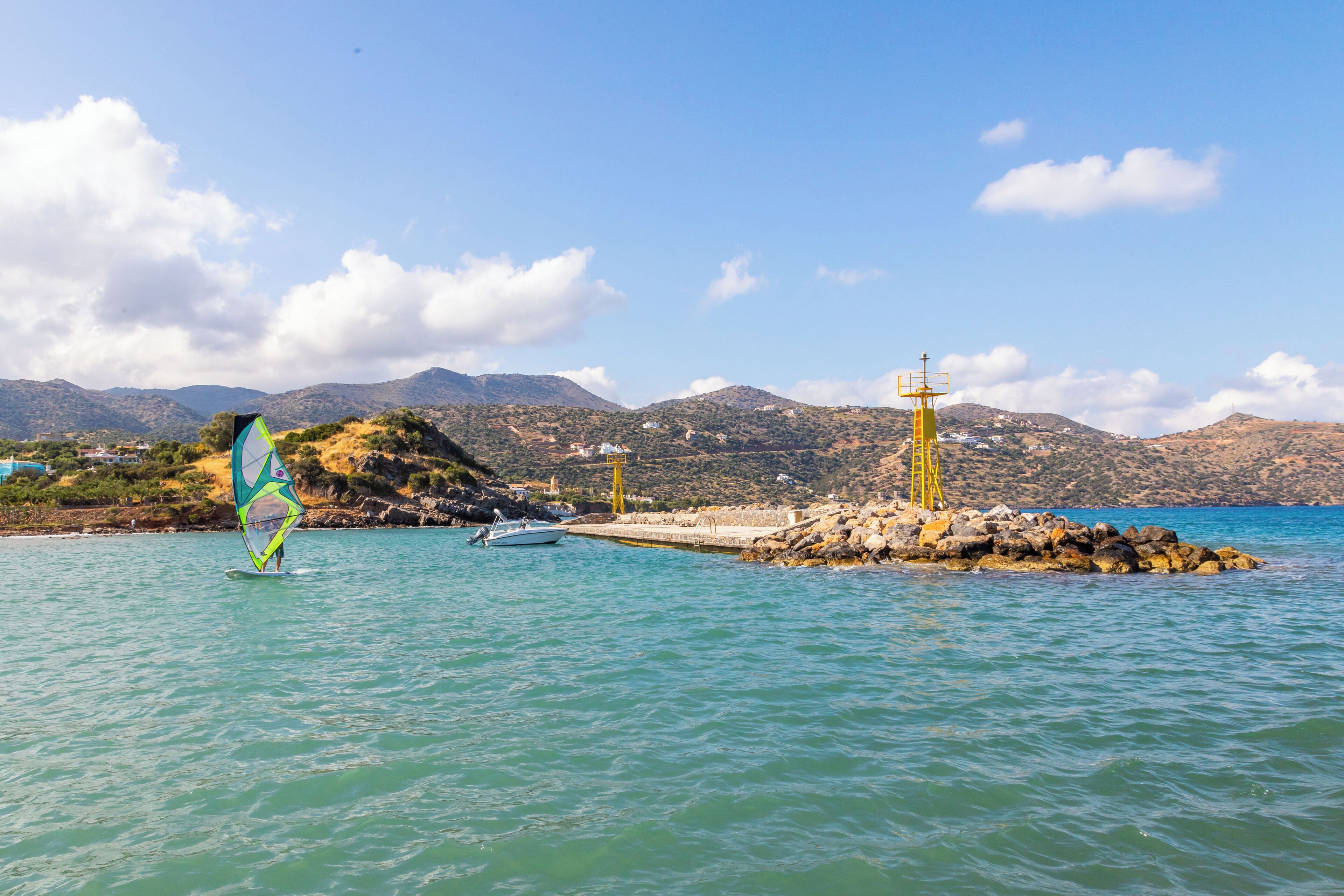 Een kustlandschap met een windsurfplank, een klein bootje en rotsformaties.