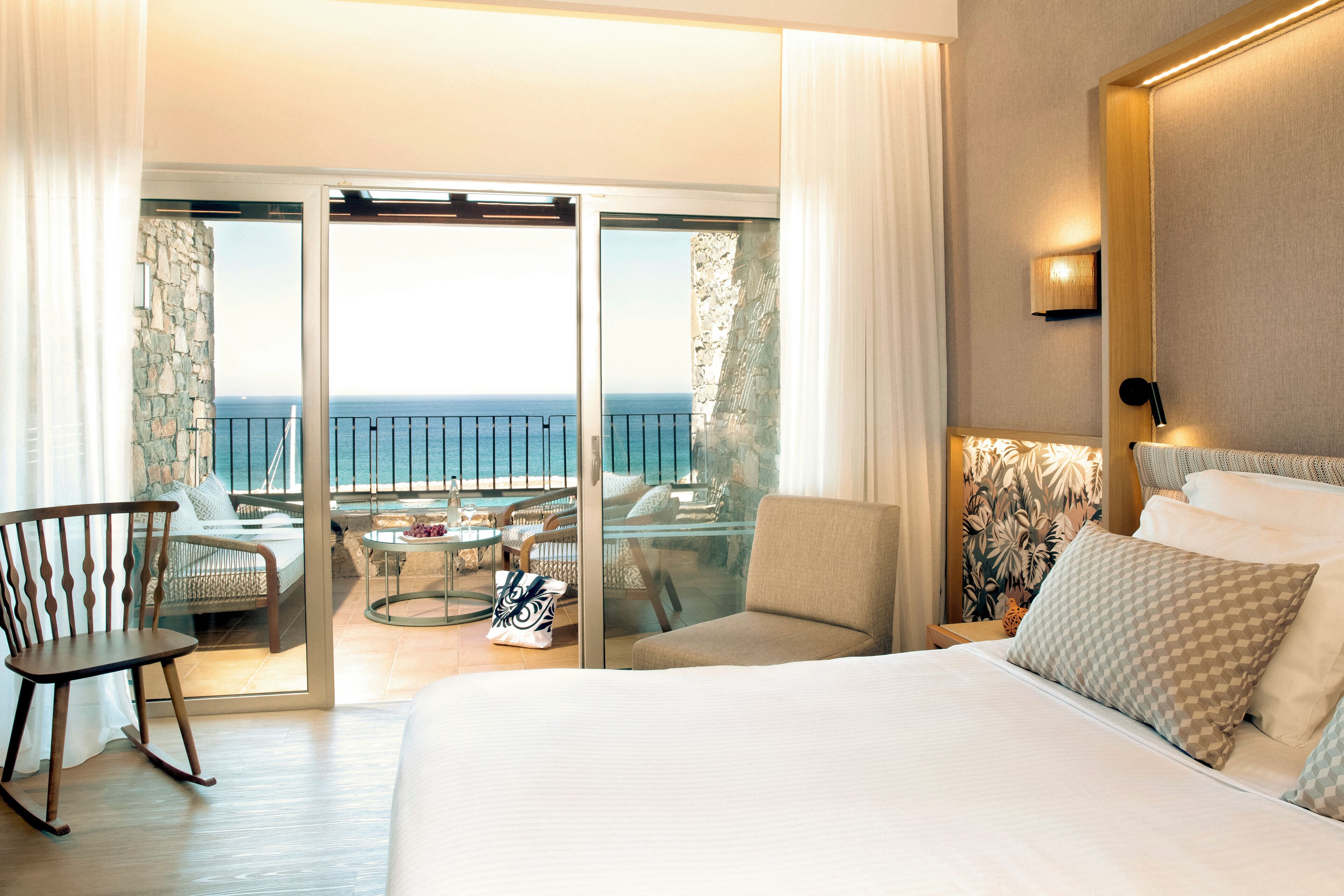 Une chambre d’hôtel avec un lit, une chaise, une petite table et un balcon donnant sur la mer.