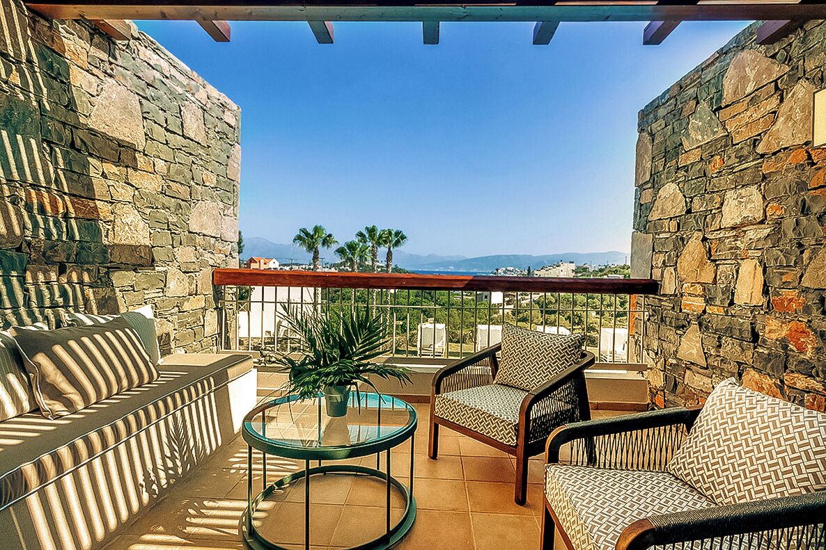 A balcony with stone walls, a sofa, two chairs, and a glass table.