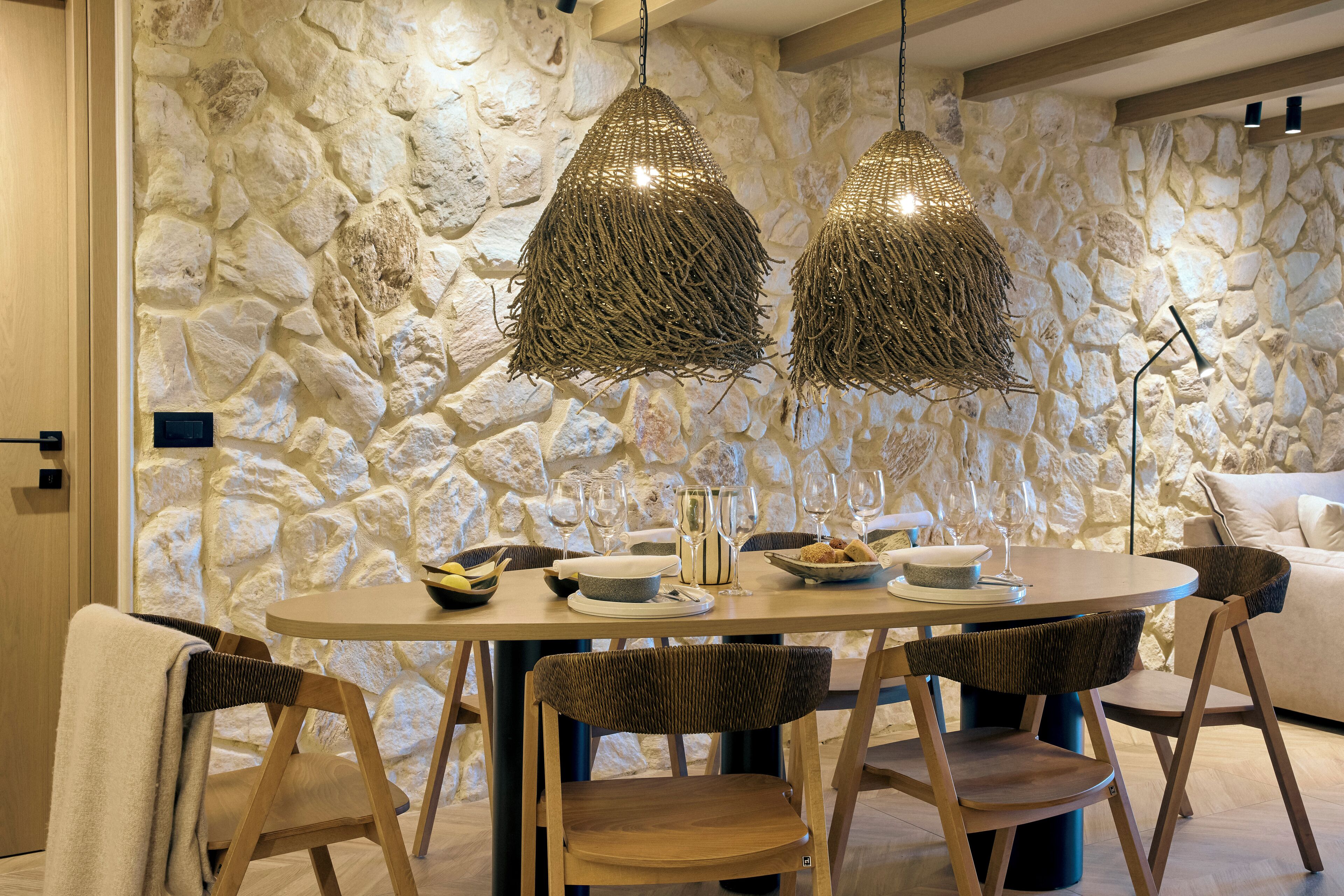 Un comedor con un fondo de pared de piedra, una mesa redonda dispuesta con platos, vasos y un cuenco de fruta.