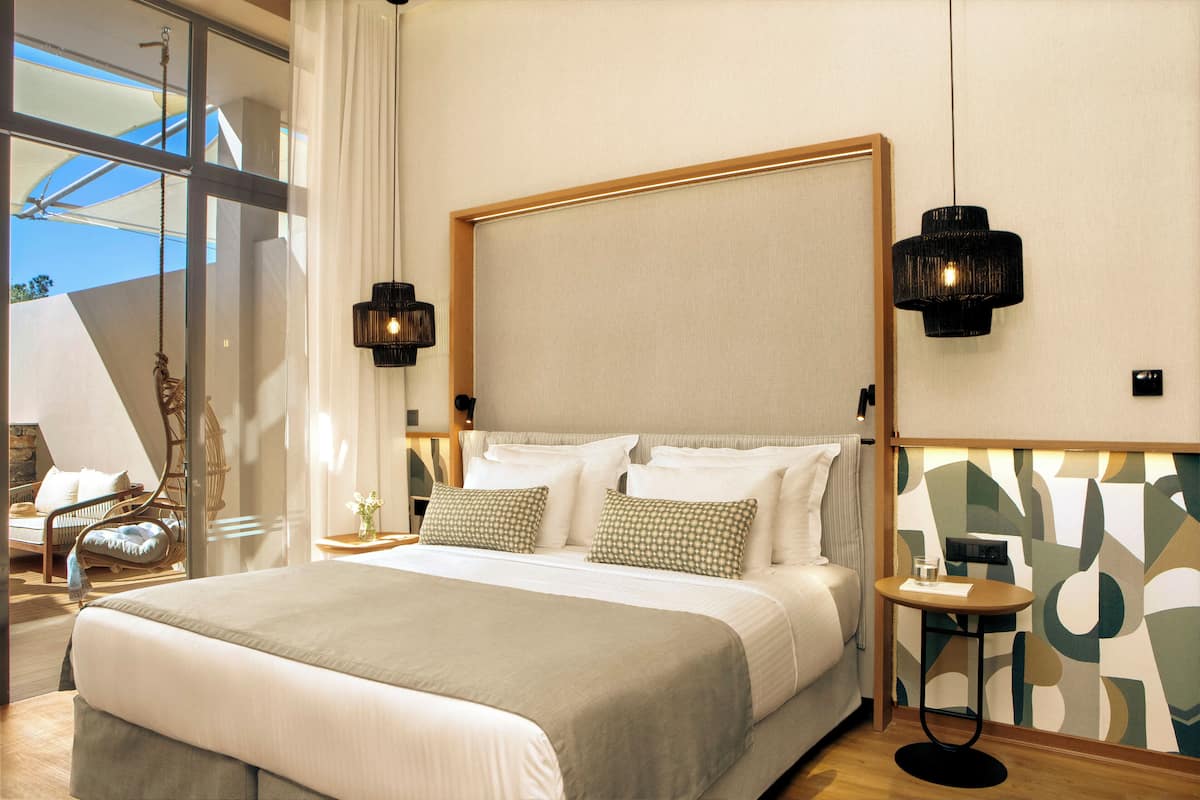 Habitación de hotel moderna con una cama grande, una mesita pequeña y vistas a través de un ventanal.