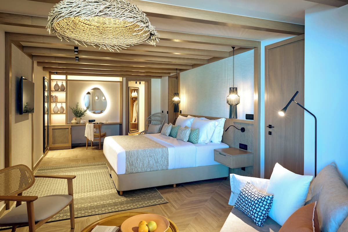 Una habitación de hotel moderna con una cama grande, mesitas de noche, un escritorio y un área de descanso.