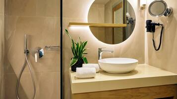 A modern bathroom with a round mirror, a sink, a handheld showerhead, and a potted plant.